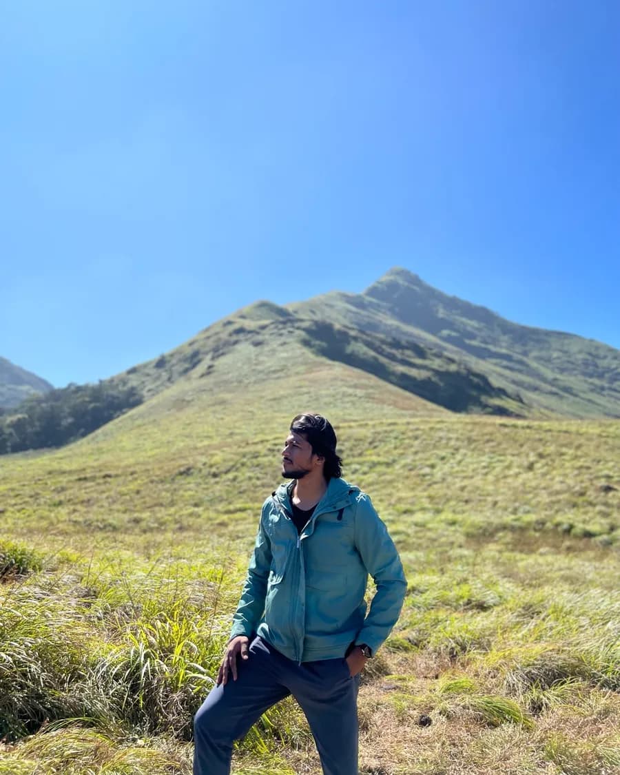 Sandeep on a grassy slope below a mountain peak