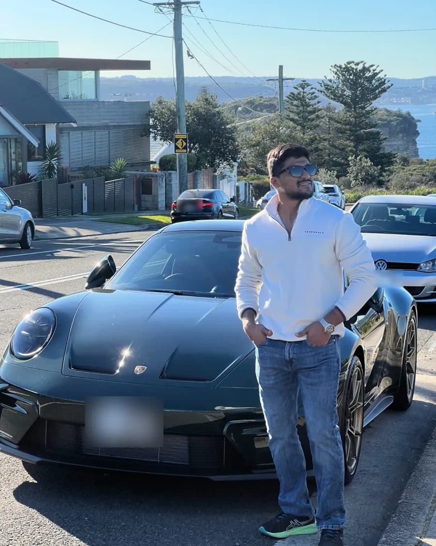 Sandeep standing beside a sports car on a coastal street