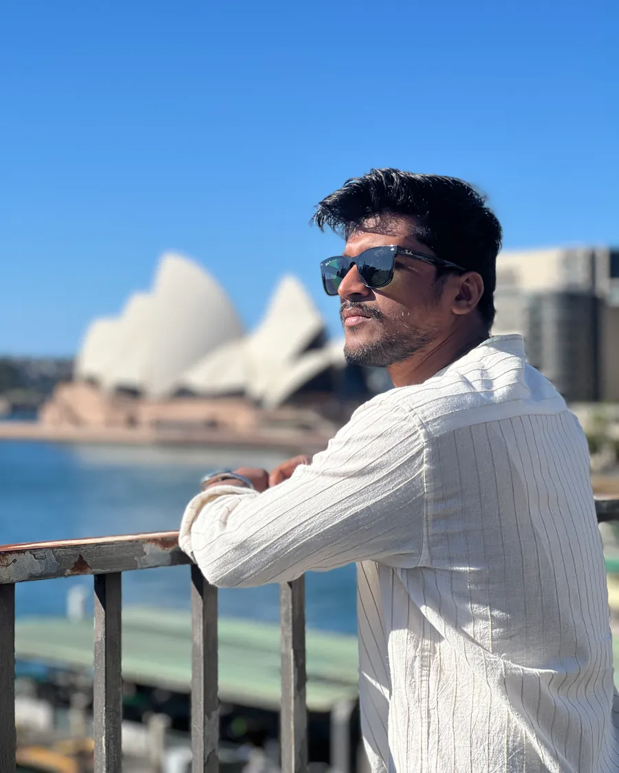 Sandeep leaning on a railing with the Sydney Opera House behind him